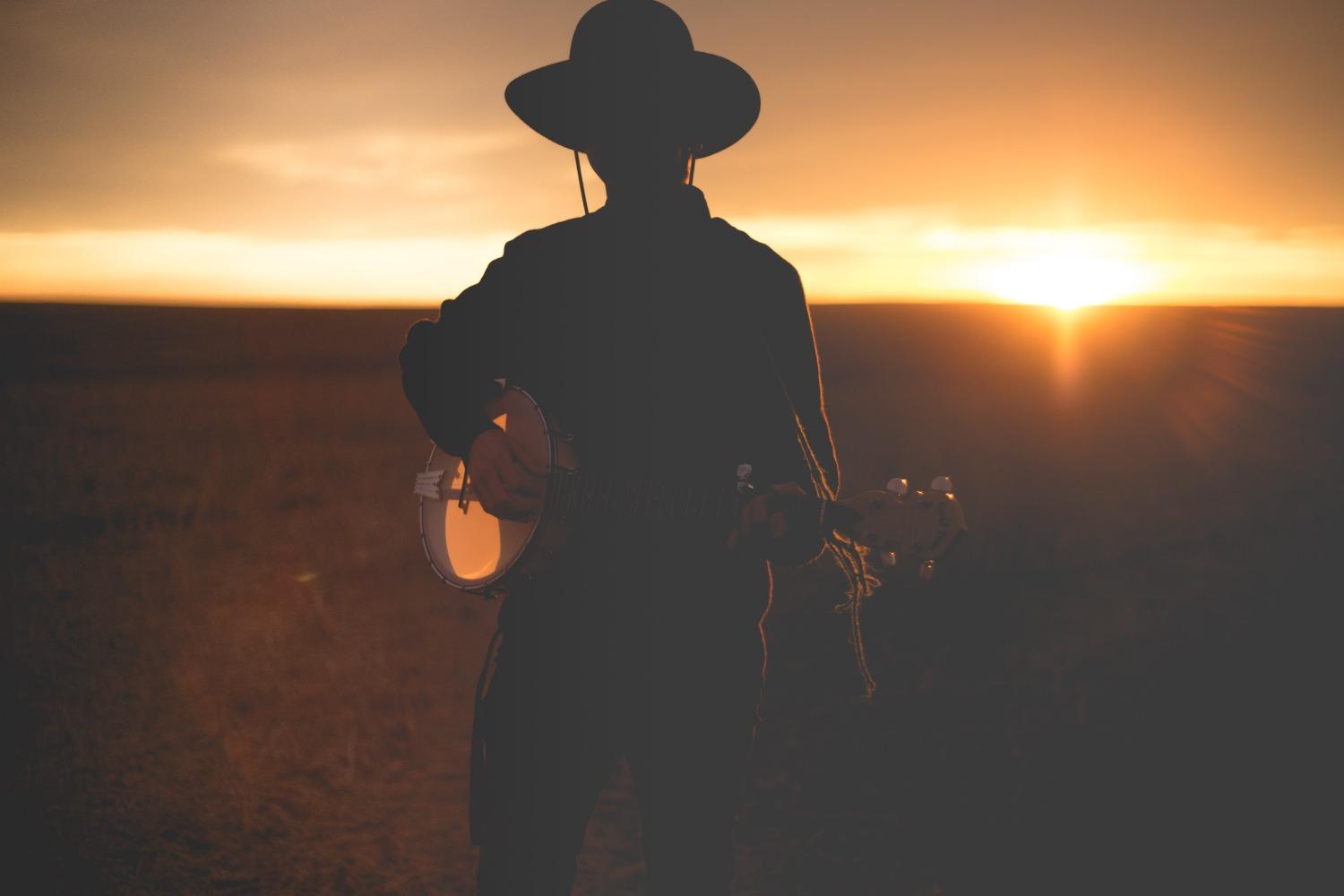 A banjo player in a field at sunset