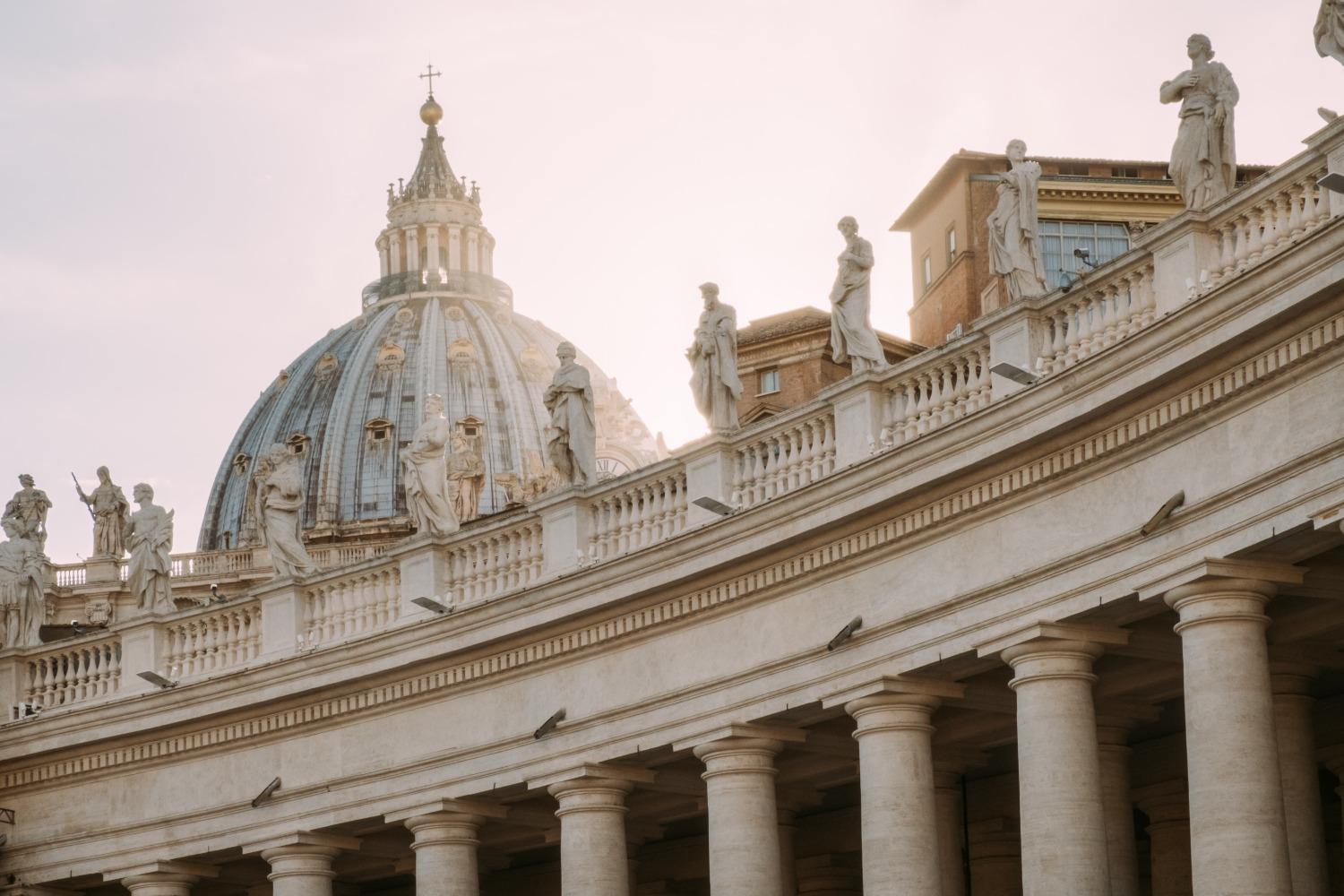 The cupola of St. Peter&#039;s Basilica rises over statues of saints on the colonnade