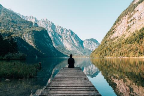 A man on a dock looking over a lake in the mountains