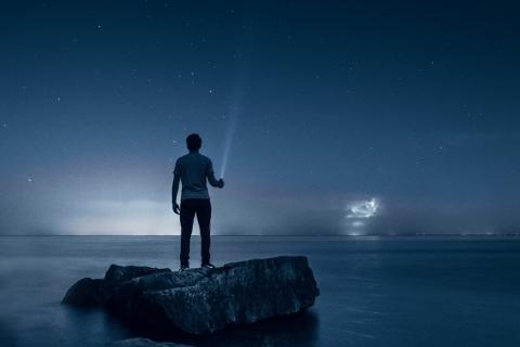 A man shining a flashlight into the night sky